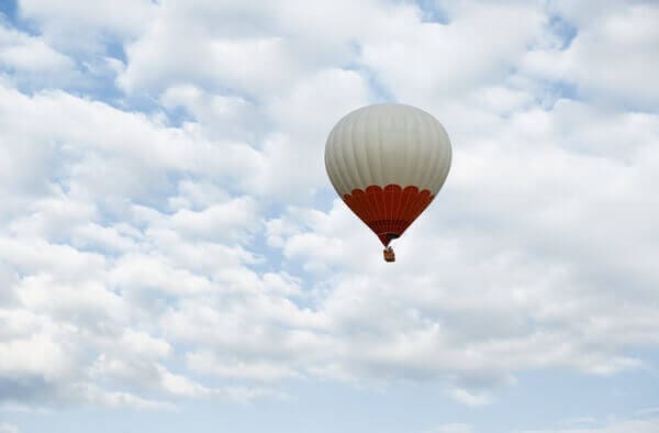 A serene hot air balloon floating in the vast blue sky amidst fluffy clouds, representing the peaceful yet exhilarating things to do in the Adelaide Hills.