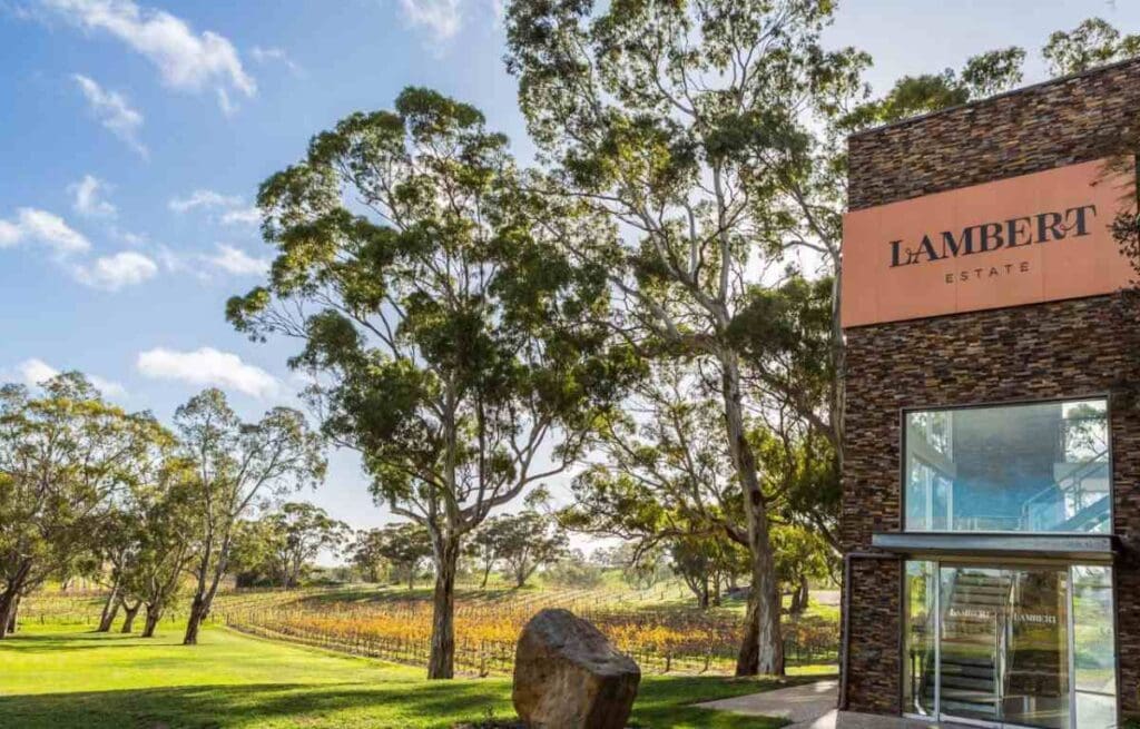 The modern entrance of Lambert Estate Winery in Barossa Valley, surrounded by tall eucalyptus trees and lush vineyards under a partly cloudy sky. This image is part of the Barossa Valley wineries map, showcasing the diverse and scenic locations featured in the blog post about exploring Australia's famous wine regions.