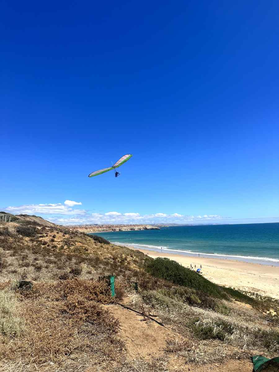 maslin beach Hang glider soaring over the scenic coastline of Maslin Beach with golden sand, clear blue skies, and turquoise water, highlighting why it’s one of the top beaches in Fleurieu Peninsula.