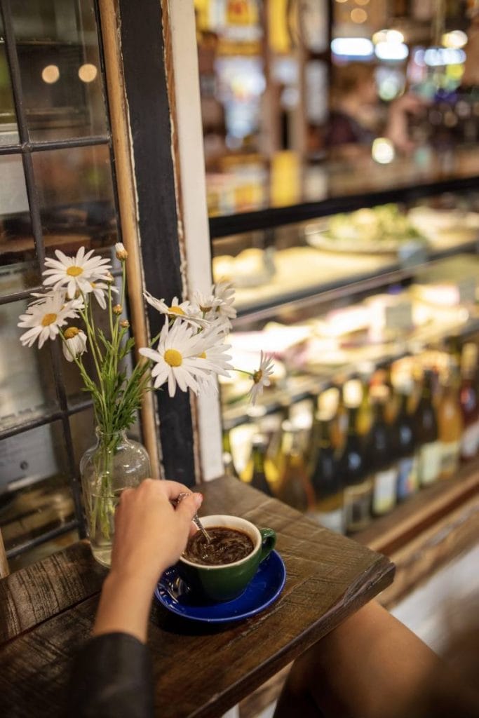 Close-up of a hand stirring coffee in a café at Adelaide Central Market, with a glass display of food and drinks in the background. The market is one of the oldest cultural landmarks in Adelaide and remains a favourite among visitors exploring Adelaide’s historic attractions.