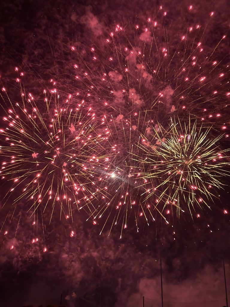 A vibrant display of pink and gold fireworks bursts across the night sky during Australia Day celebrations in Adelaide. The colourful streaks and smoky backdrop capture the festive energy of the city's annual event.