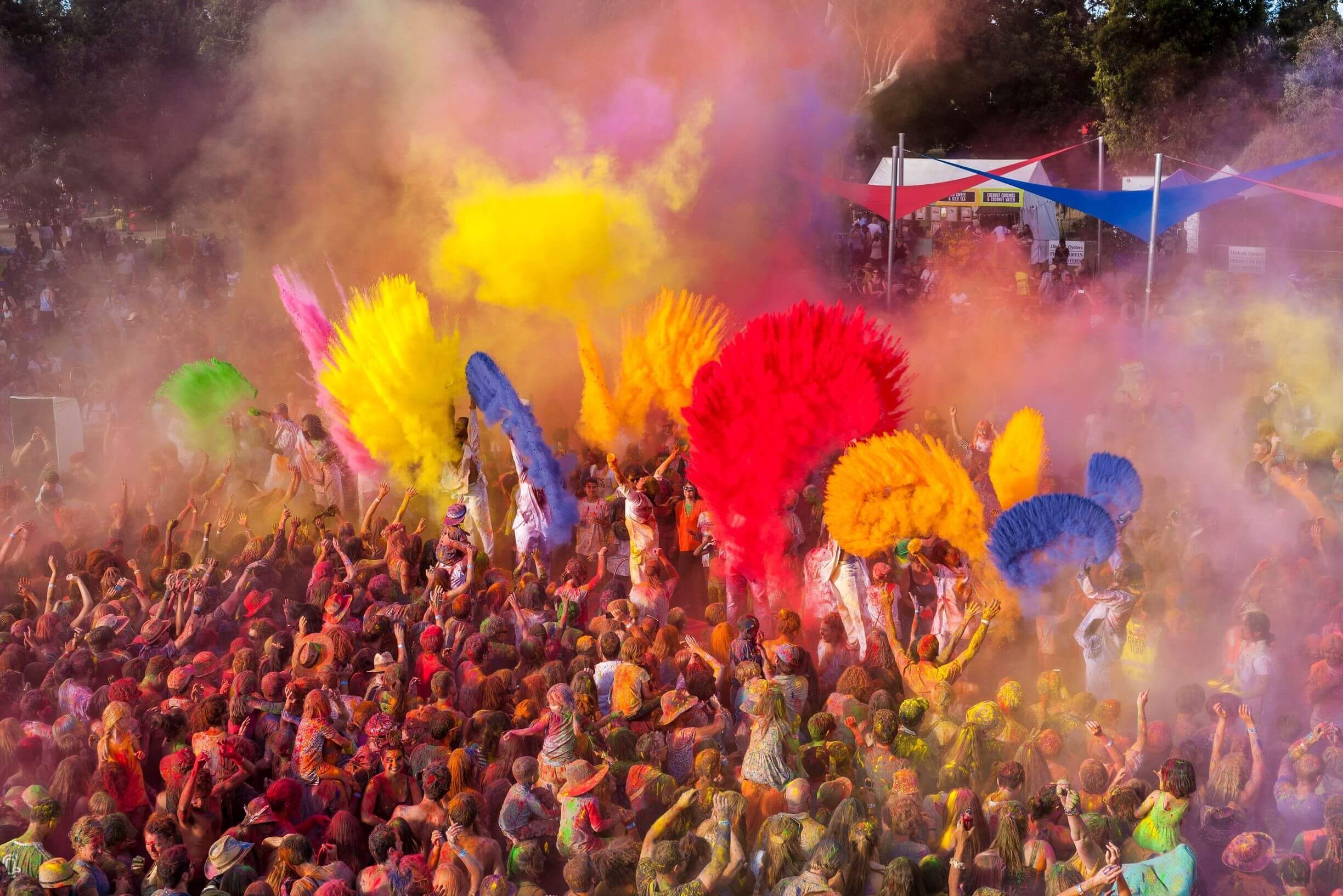 Festival crowd celebrating with vibrant clouds of coloured powder in the air at WOMADelaide 2026, capturing the lively, multicultural atmosphere and immersive experiences.
