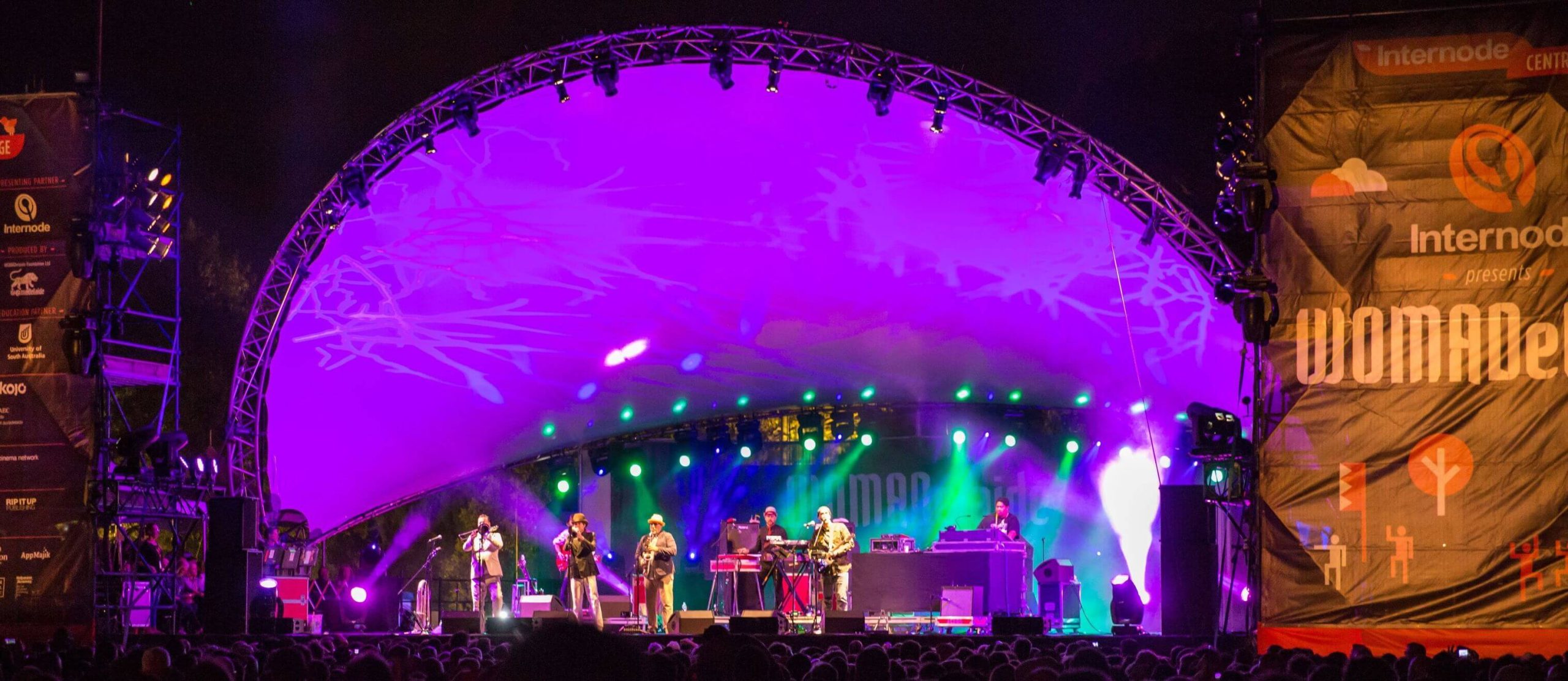 WOMADelaide 2026 live music performance on the main stage in Adelaide’s Botanic Park, with vibrant purple and green lights illuminating the band and a large crowd gathered in front, showcasing the energetic festival atmosphere featured in the blog post.