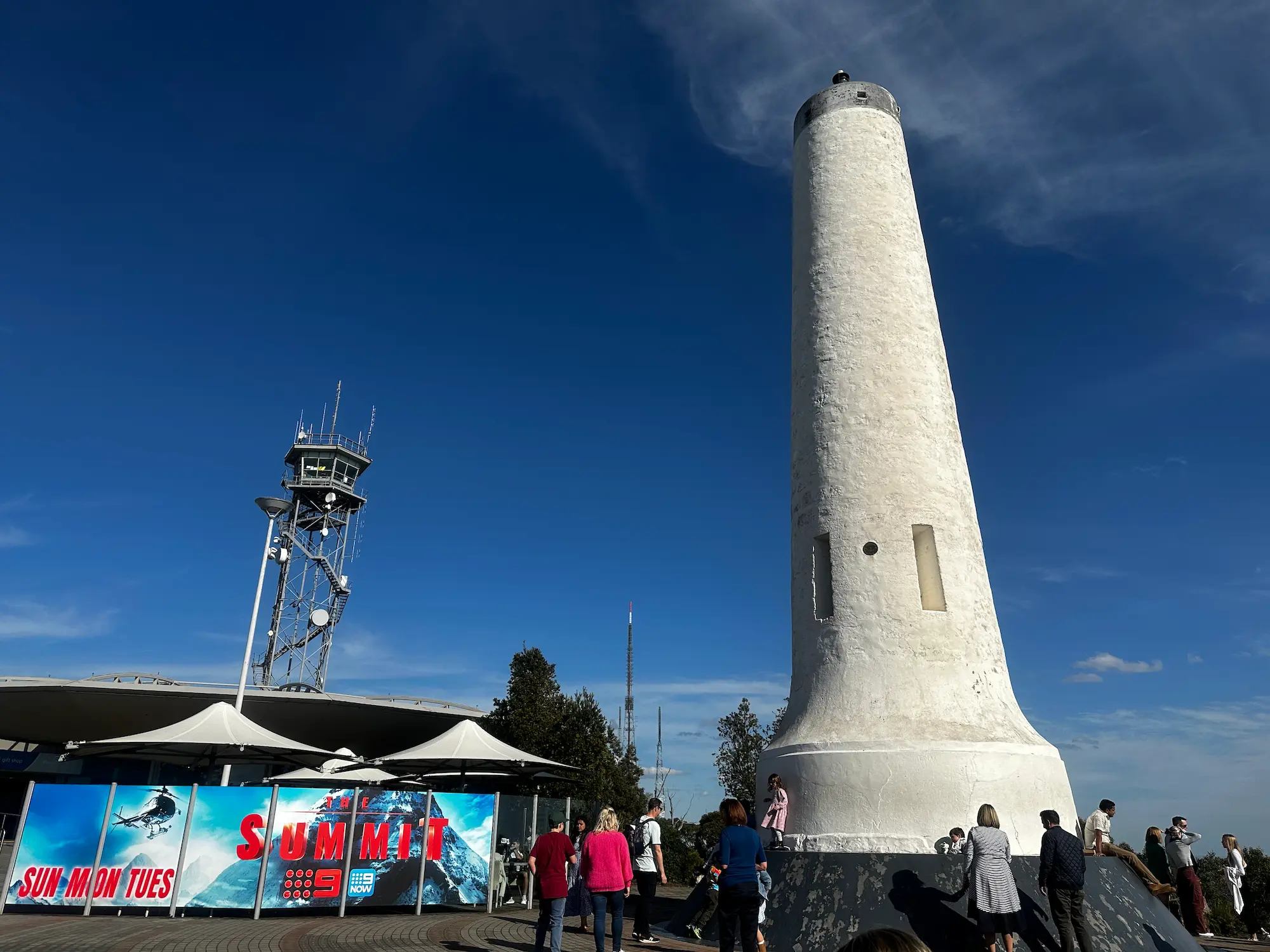 The white Mount Lofty Summit lookout tower rises against a deep blue sky as visitors gather around the viewing area overlooking the Adelaide Hills. Mount Lofty Summit is one of the most popular places to visit on day trips from Adelaide, offering panoramic views across the city and coastline.