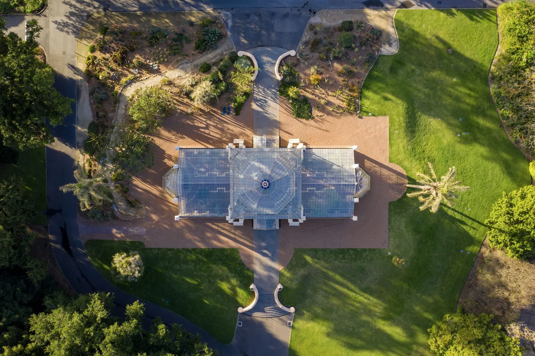 Aerial view looking straight down over the glass roof of a conservatory surrounded by green lawns and landscaped gardens at Adelaide Botanic Garden. The garden is a peaceful nature stop to include on an Adelaide itinerary.