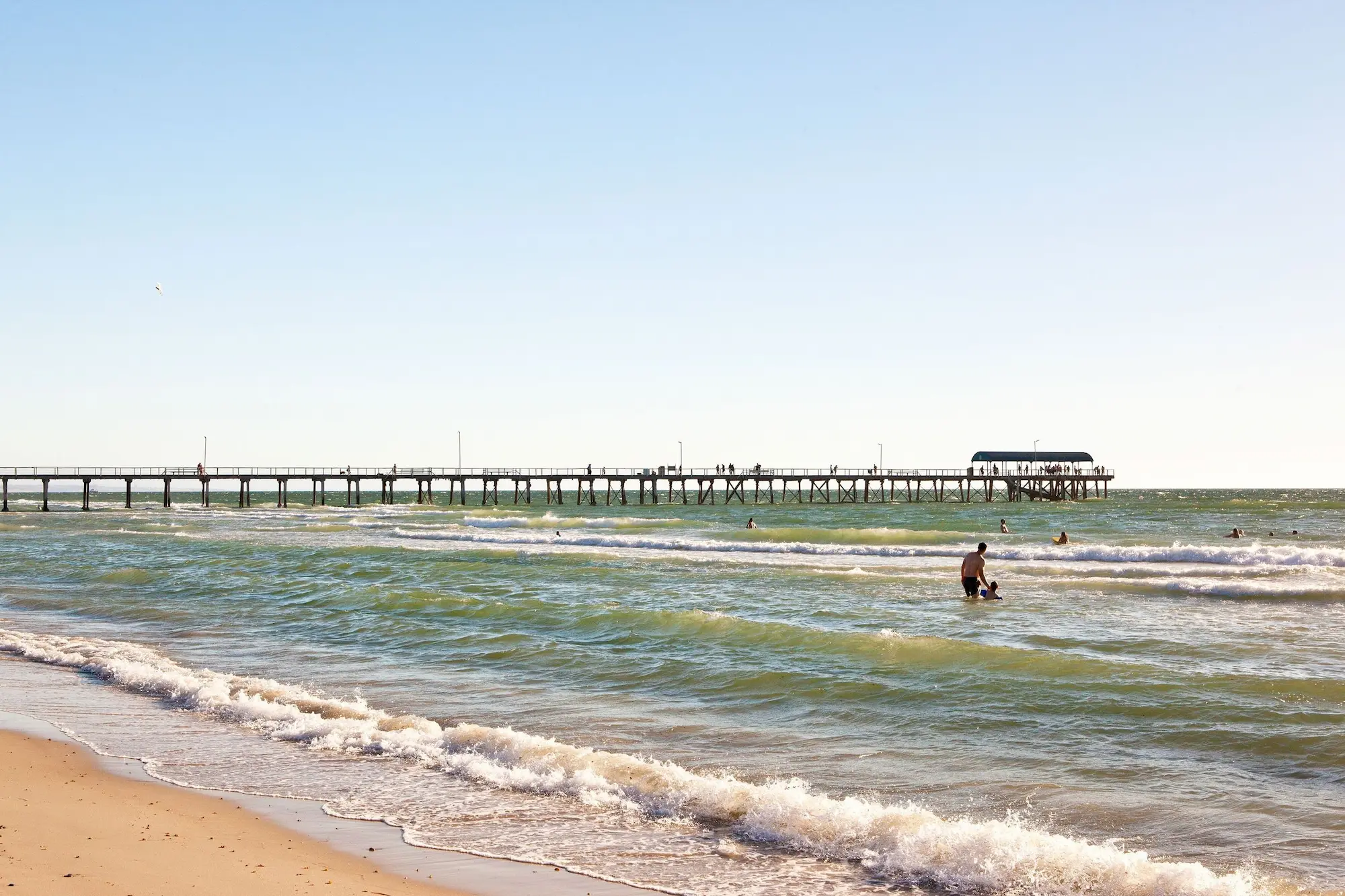 Gentle waves roll onto the sand at Henley Beach as swimmers enjoy the water beside the long Henley Beach Jetty. This seaside stop offers a relaxing change of pace while exploring Adelaide.
