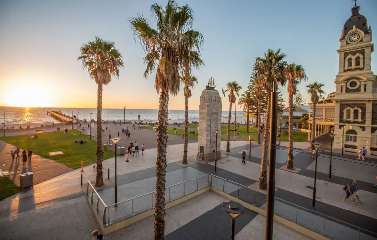 Sunset over Glenelg Beach with palm trees. the jetty. seaside lawns. and the historic Town Hall surrounding Moseley Square. Glenelg is a popular coastal stop for an evening by the sea during three days in Adelaide.